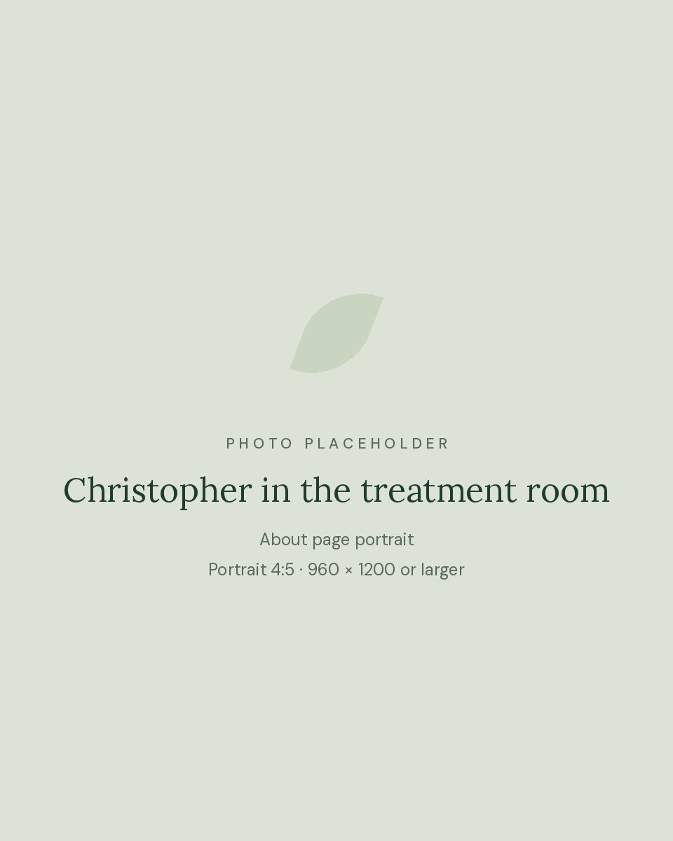 Christopher DeLucca, LMT, standing beside a massage table in his warm, plant-filled treatment room